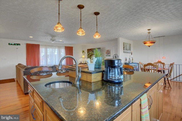 kitchen with light wood-style flooring, open floor plan, hanging light fixtures, a textured ceiling, and a sink