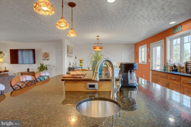 kitchen with a sink, open floor plan, a textured ceiling, and decorative light fixtures