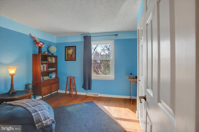 sitting room featuring baseboards, a textured ceiling, visible vents, and wood finished floors