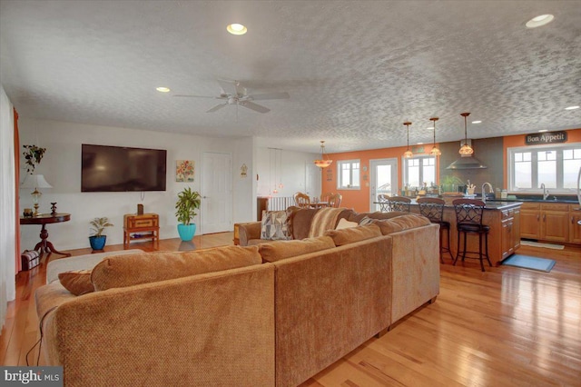 living area featuring light wood-type flooring, ceiling fan, a textured ceiling, and recessed lighting