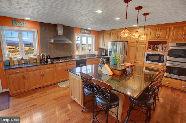 kitchen featuring appliances with stainless steel finishes, a sink, light wood-type flooring, wall chimney range hood, and backsplash