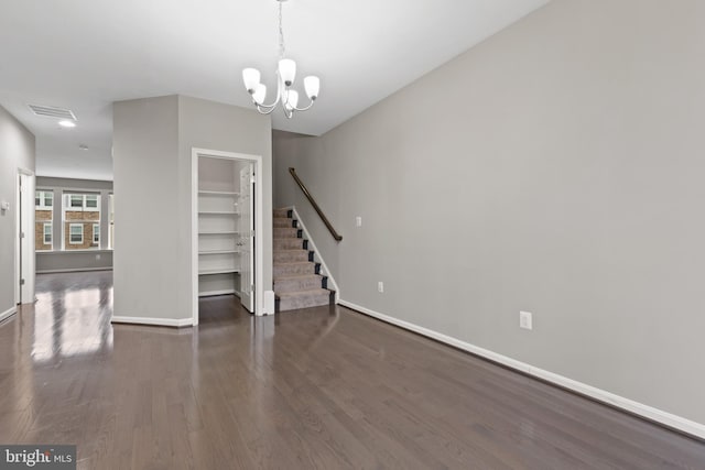 unfurnished living room with a chandelier, baseboards, wood finished floors, and stairs