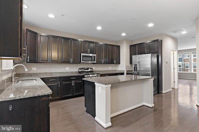 kitchen featuring a center island, light stone countertops, appliances with stainless steel finishes, and a sink