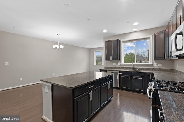 kitchen featuring a kitchen island, baseboards, appliances with stainless steel finishes, dark wood-style floors, and a sink