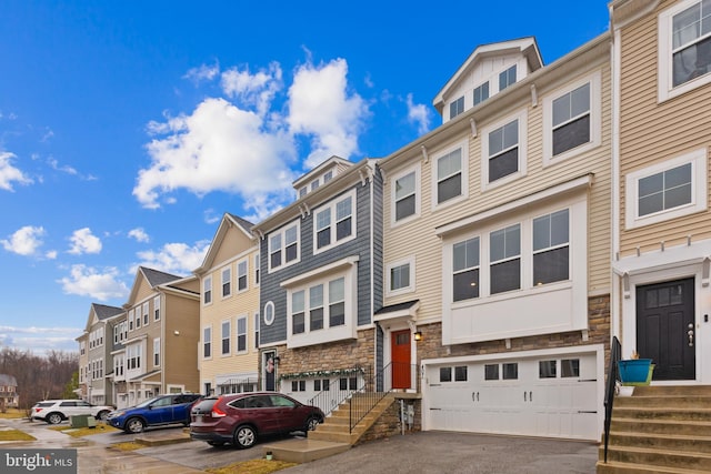 townhome / multi-family property featuring a residential view, stone siding, an attached garage, and aphalt driveway