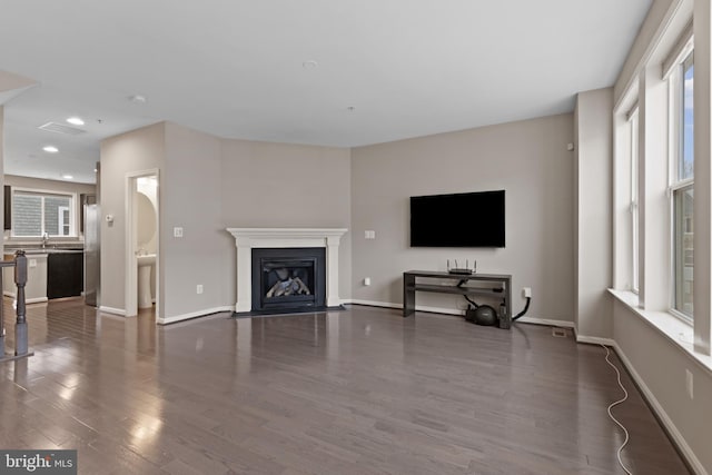 living room featuring a fireplace with flush hearth, baseboards, and dark wood-style flooring