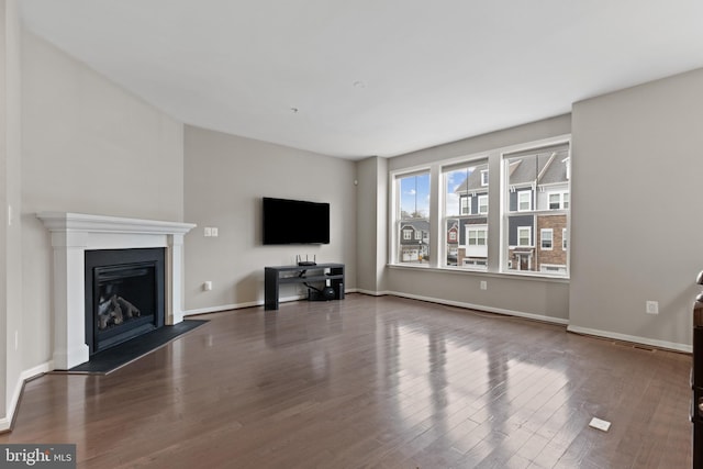 unfurnished living room featuring a glass covered fireplace, wood finished floors, and baseboards