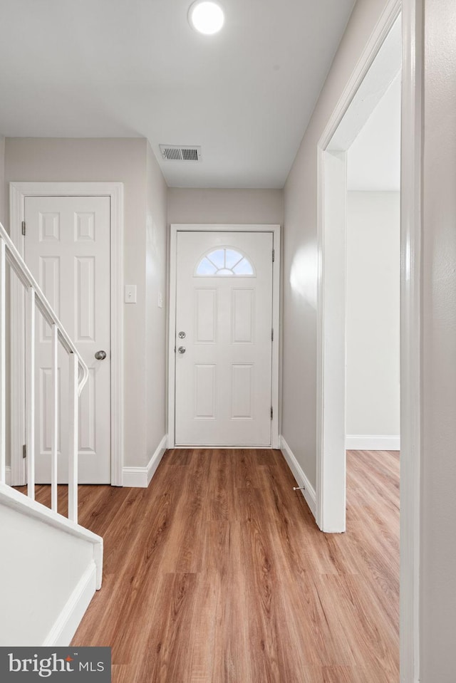 foyer with stairs, light wood-type flooring, visible vents, and baseboards