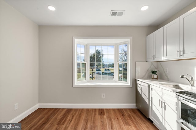 kitchen with a sink, visible vents, baseboards, light countertops, and light wood finished floors