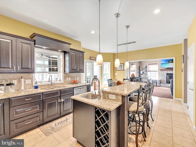 kitchen with dark brown cabinetry, decorative backsplash, a kitchen breakfast bar, stainless steel dishwasher, and a sink