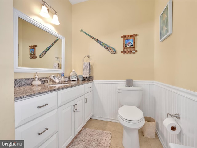 half bath featuring a wainscoted wall, vanity, toilet, and tile patterned floors