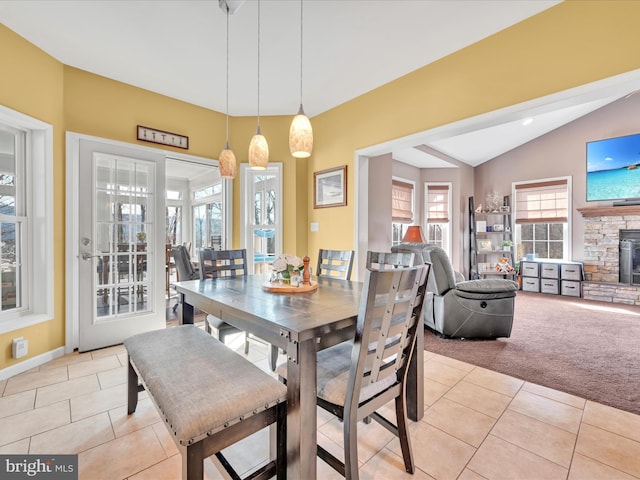 dining room featuring lofted ceiling, light tile patterned floors, a fireplace, and light colored carpet