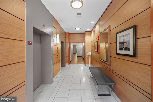 corridor with light tile patterned floors, visible vents, elevator, and wood walls