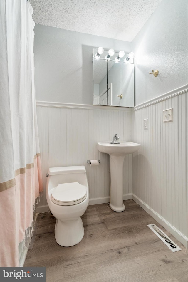 bathroom with a wainscoted wall, visible vents, toilet, a textured ceiling, and wood finished floors