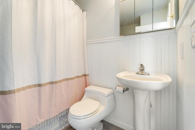 full bath with a wainscoted wall, toilet, and a shower with curtain