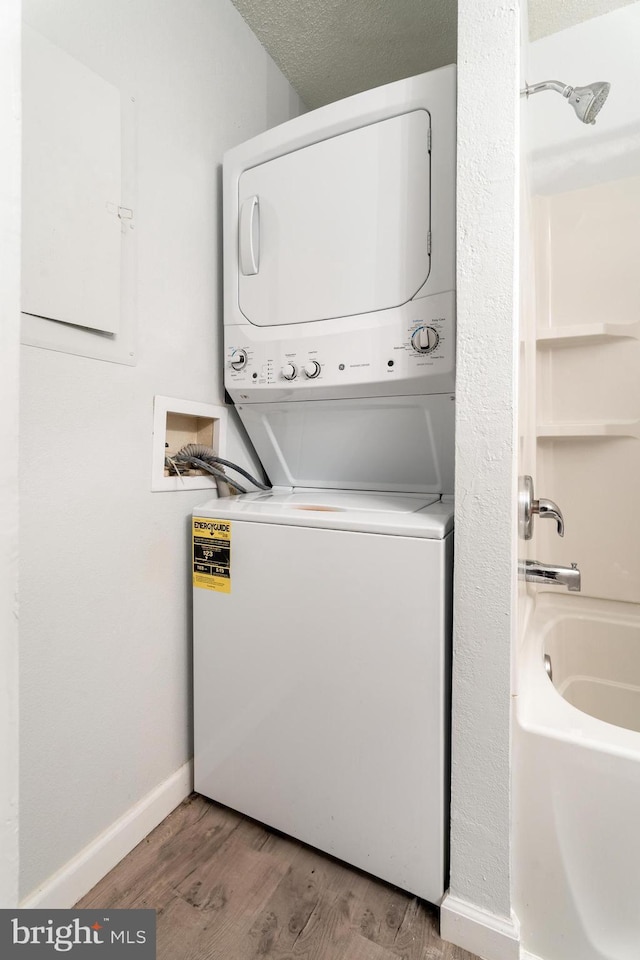 laundry area with baseboards, laundry area, wood finished floors, and stacked washer / drying machine