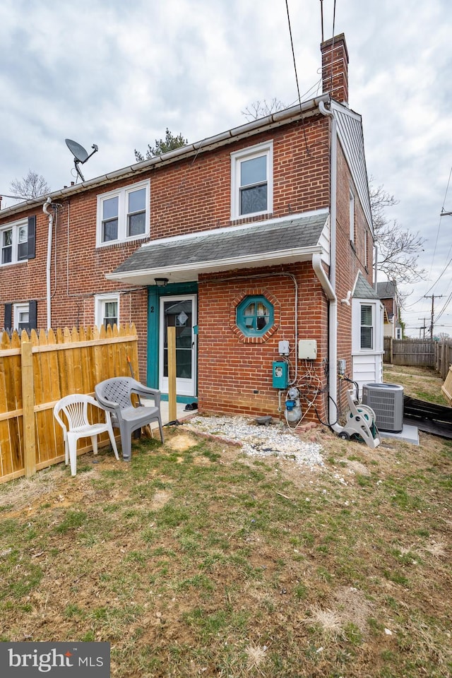 rear view of property with brick siding, fence, a lawn, and central air condition unit