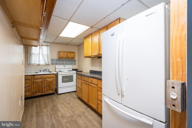 kitchen featuring light wood finished floors, tasteful backsplash, a paneled ceiling, a sink, and white appliances