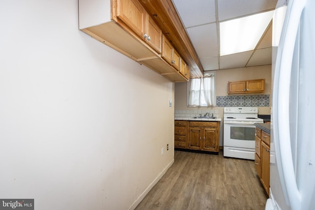 kitchen featuring white appliances, decorative backsplash, brown cabinets, a paneled ceiling, and a sink