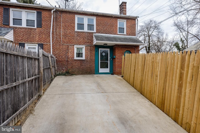 back of house with a patio, brick siding, fence, roof with shingles, and a chimney