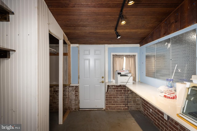 mudroom featuring wood ceiling, rail lighting, unfinished concrete flooring, and brick wall