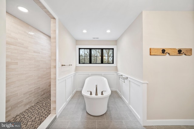 bathroom with visible vents, wainscoting, a freestanding bath, a walk in shower, and a decorative wall