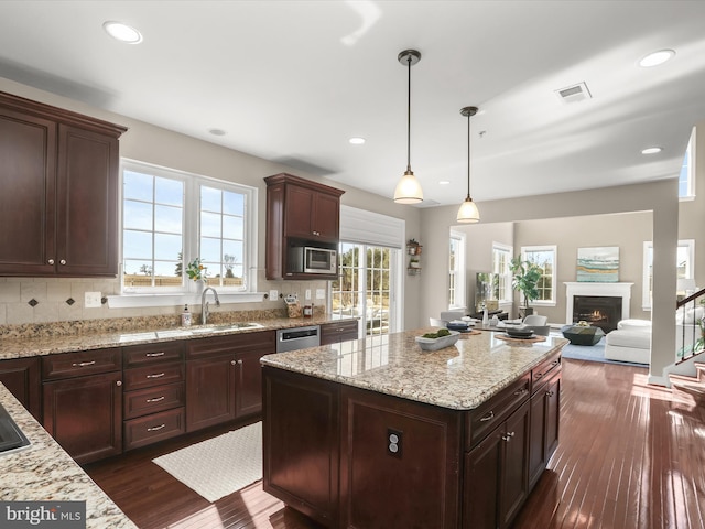 kitchen with visible vents, a sink, a warm lit fireplace, dark wood finished floors, and stainless steel appliances