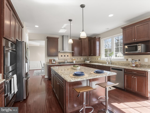 kitchen with appliances with stainless steel finishes, dark wood-style floors, a center island, and wall chimney range hood