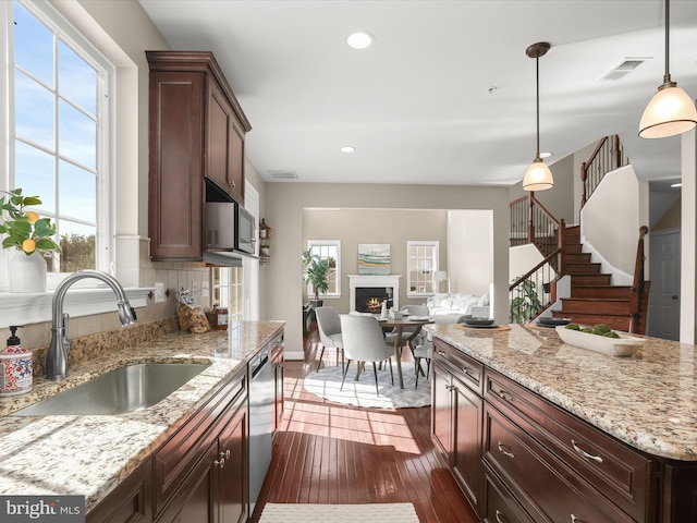 kitchen featuring dark wood finished floors, a warm lit fireplace, stainless steel appliances, a sink, and open floor plan