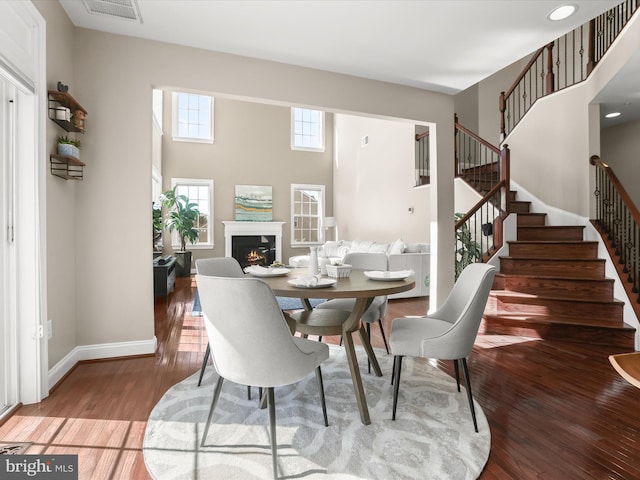 dining area with visible vents, baseboards, stairs, hardwood / wood-style flooring, and a glass covered fireplace