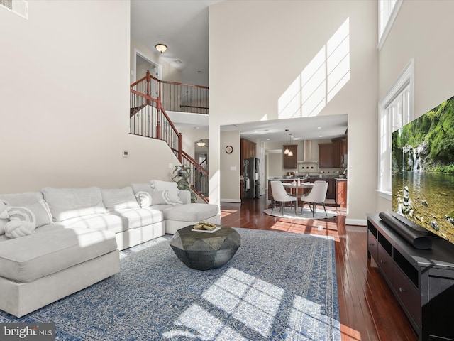 living area with visible vents, stairway, a high ceiling, and dark wood-style flooring