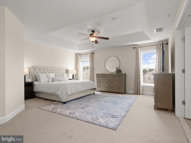 bedroom with a tray ceiling, carpet flooring, baseboards, and visible vents