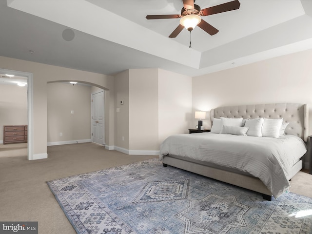 bedroom with baseboards, arched walkways, a raised ceiling, and light carpet