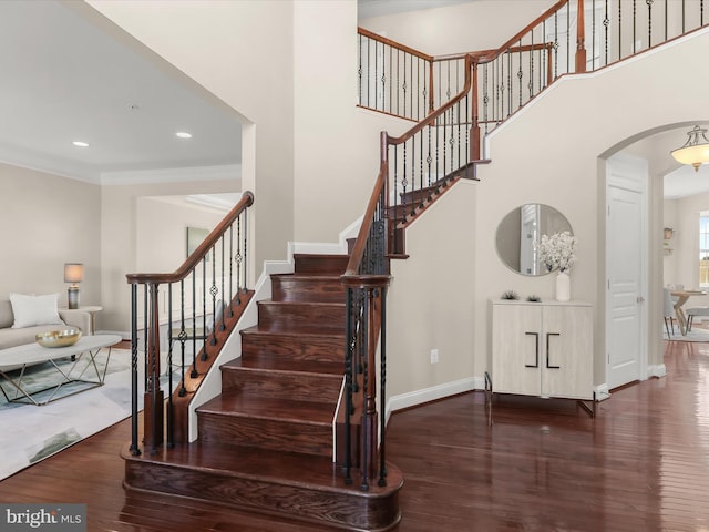 stairs with arched walkways, crown molding, baseboards, and wood finished floors