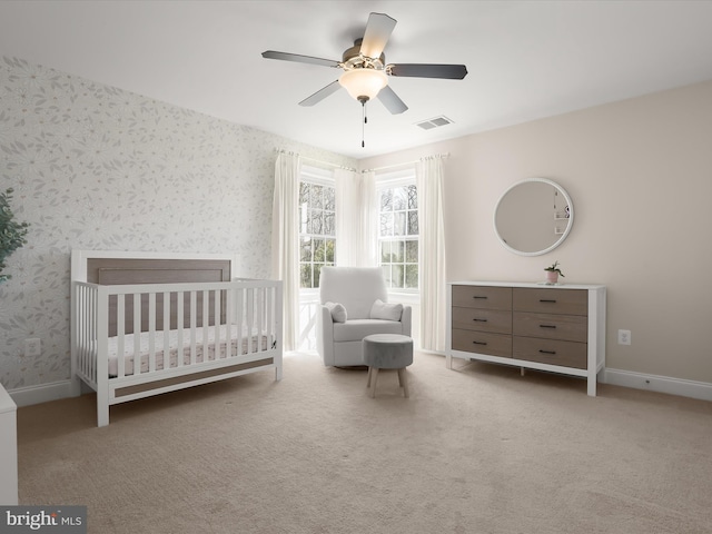 unfurnished bedroom with visible vents, a crib, carpet floors, wallpapered walls, and baseboards