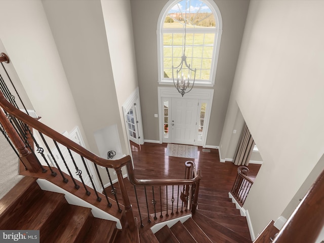 foyer entrance with stairway, wood finished floors, baseboards, a high ceiling, and a notable chandelier