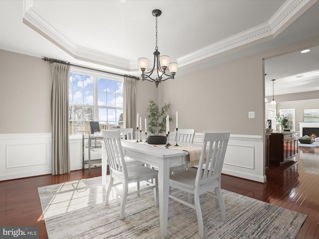 dining room featuring a tray ceiling, wood-type flooring, a lit fireplace, and crown molding