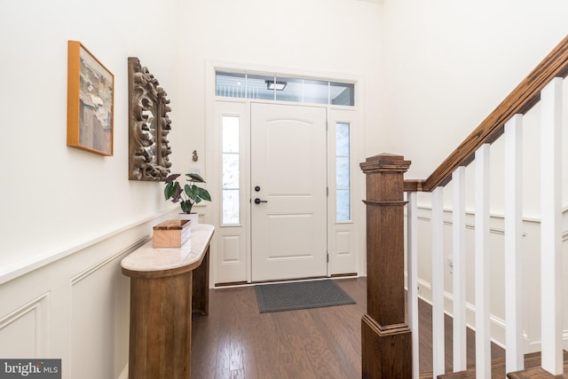 foyer with stairway, dark wood-style flooring, wainscoting, and a decorative wall