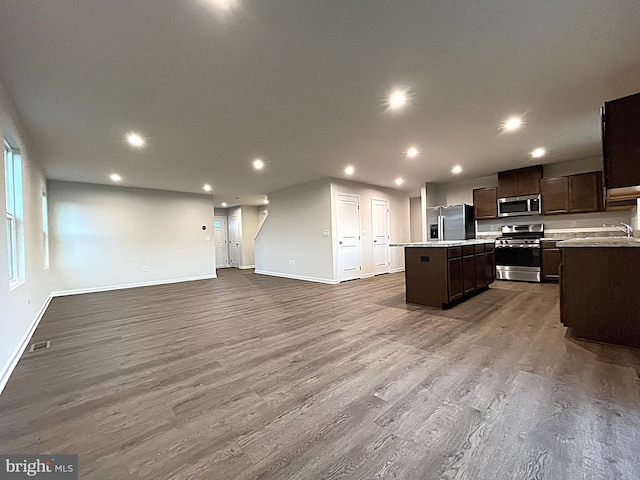 kitchen featuring appliances with stainless steel finishes, open floor plan, dark wood-type flooring, a center island, and dark brown cabinets