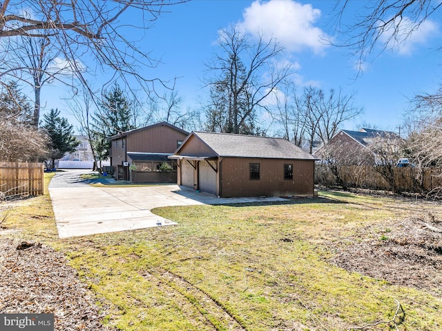 rear view of property featuring a detached garage, fence, a lawn, and an outbuilding