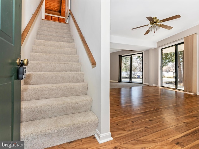 stairway featuring a ceiling fan, baseboards, and wood finished floors