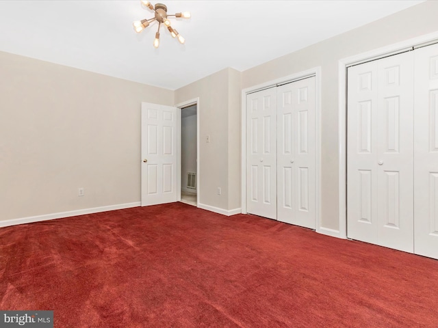 unfurnished bedroom featuring carpet floors, a notable chandelier, two closets, visible vents, and baseboards