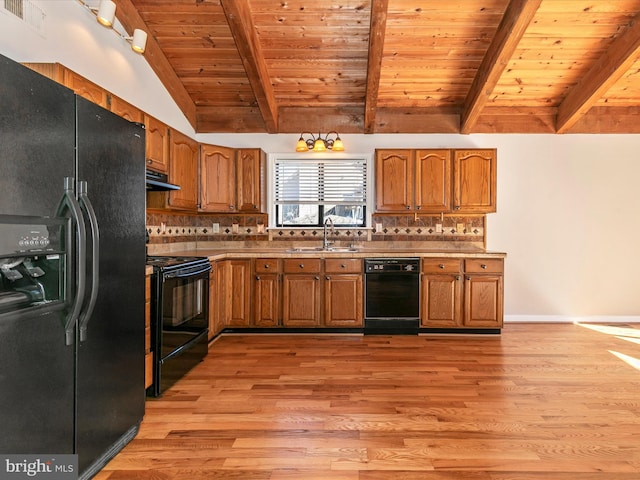 kitchen featuring vaulted ceiling with beams, under cabinet range hood, a sink, black appliances, and brown cabinetry