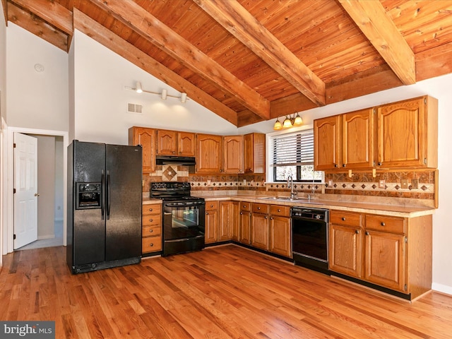 kitchen featuring light countertops, backsplash, brown cabinetry, under cabinet range hood, and black appliances