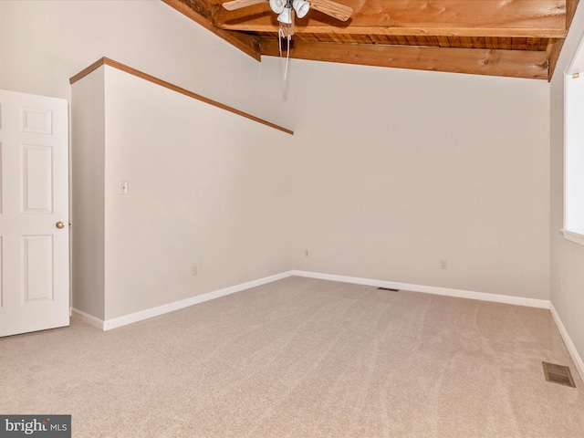 carpeted spare room featuring wood ceiling, a ceiling fan, visible vents, baseboards, and beam ceiling