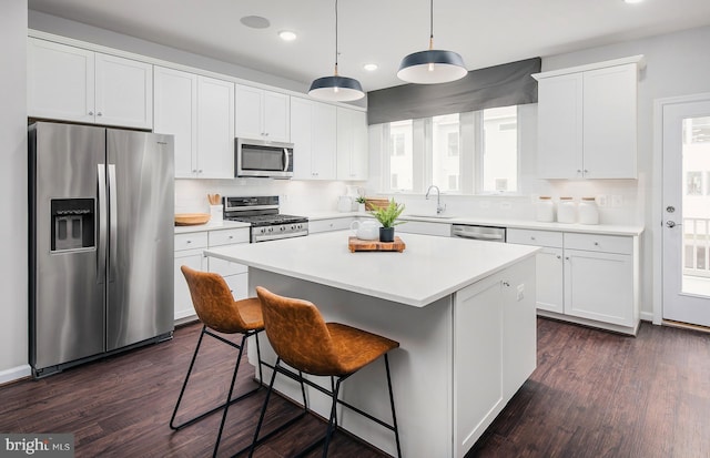 kitchen with white cabinets, a kitchen island, appliances with stainless steel finishes, light countertops, and a kitchen bar