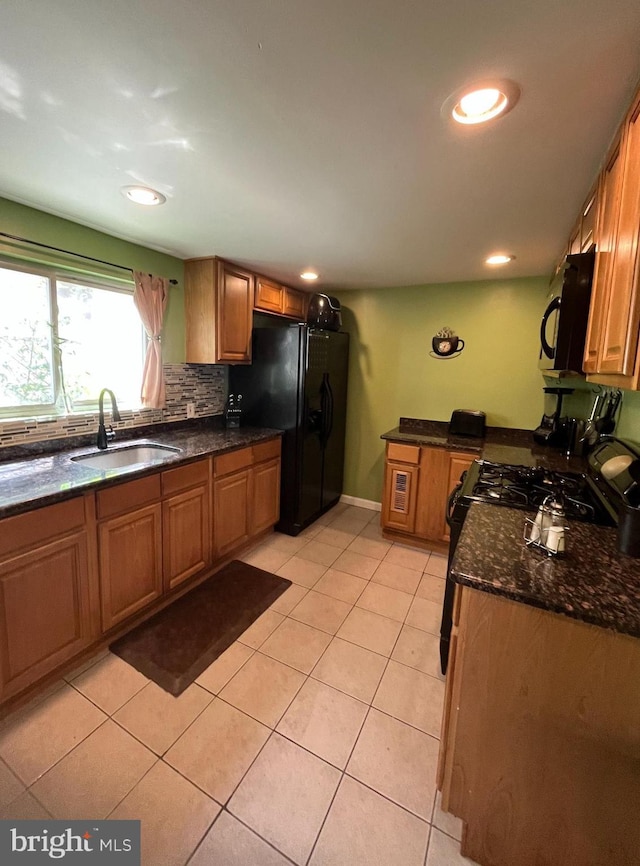 kitchen with light tile patterned floors, brown cabinetry, backsplash, black appliances, and a sink