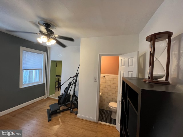 workout room with light wood-style flooring, a textured ceiling, ceiling fan, and tile walls