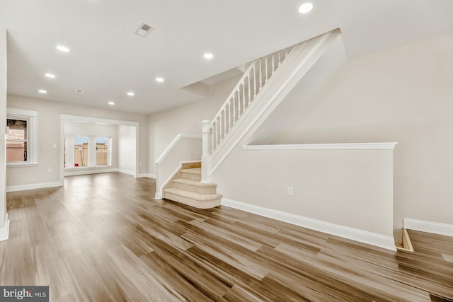 unfurnished living room featuring stairs, baseboards, wood finished floors, and recessed lighting