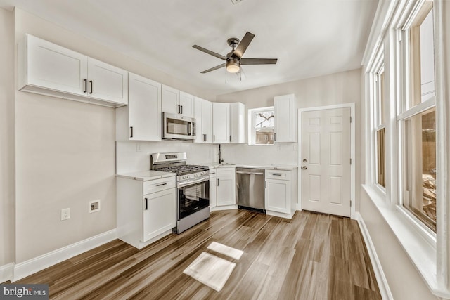 kitchen with decorative backsplash, appliances with stainless steel finishes, white cabinets, light wood-type flooring, and baseboards